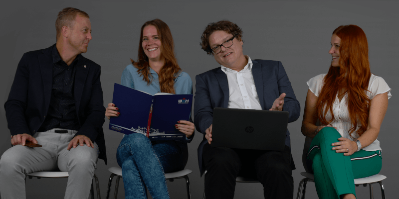 Mitarbeiter/innen sitzen auf Stühlen und lachen und reden miteinander