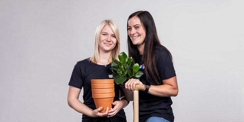 Zwei WH Mitarbeiter mit Blume, Schaufel und Blumentöpfen in den Händen