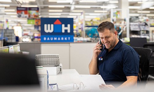 Baumarktmitarbeiter sitzt am Schreibtisch und telefoniert freudig